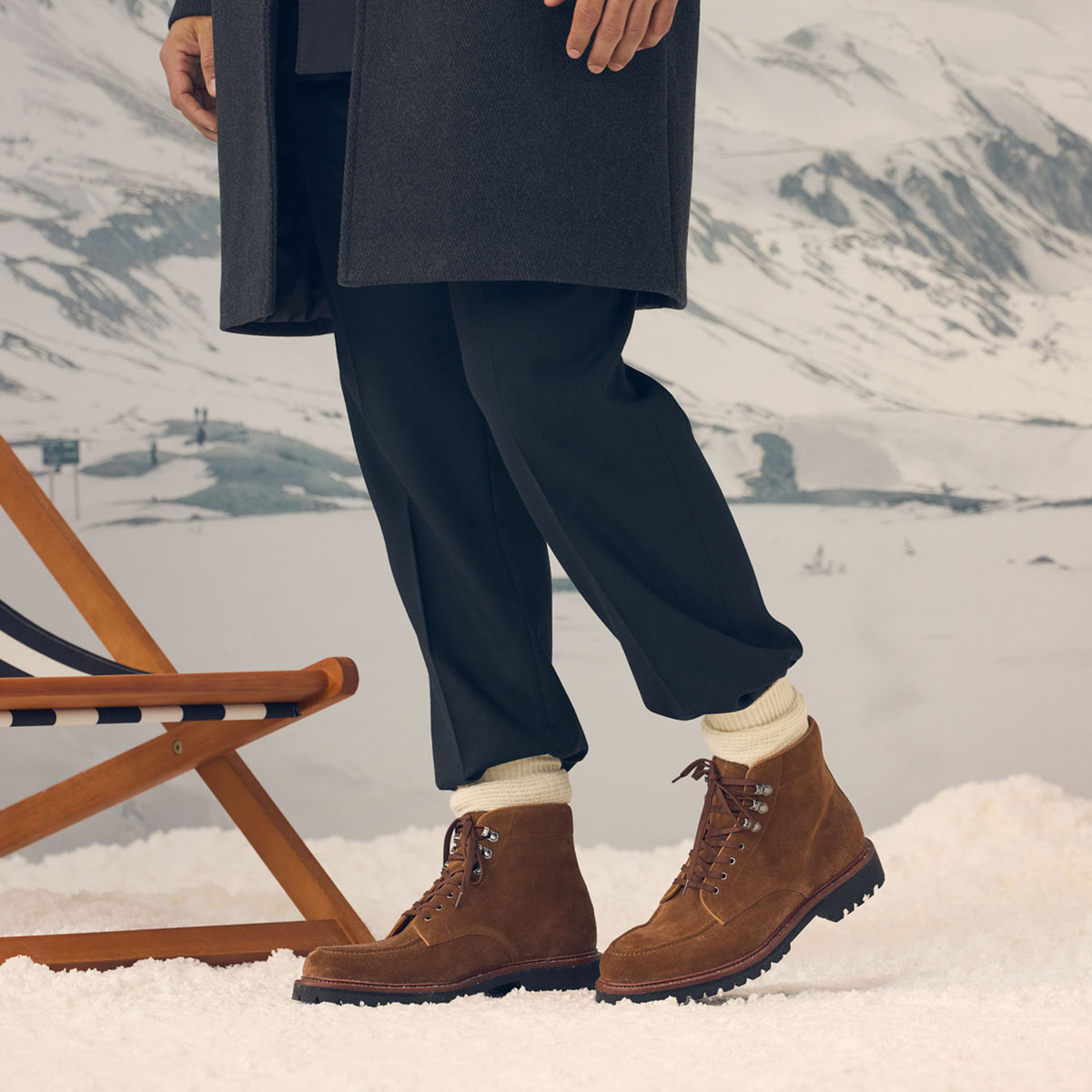 A close-up shot of a man wearing a pair of brown boots against a snowy backdrop