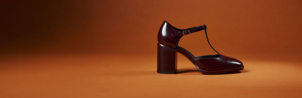 A single burgundy heeled loafer against an orange background