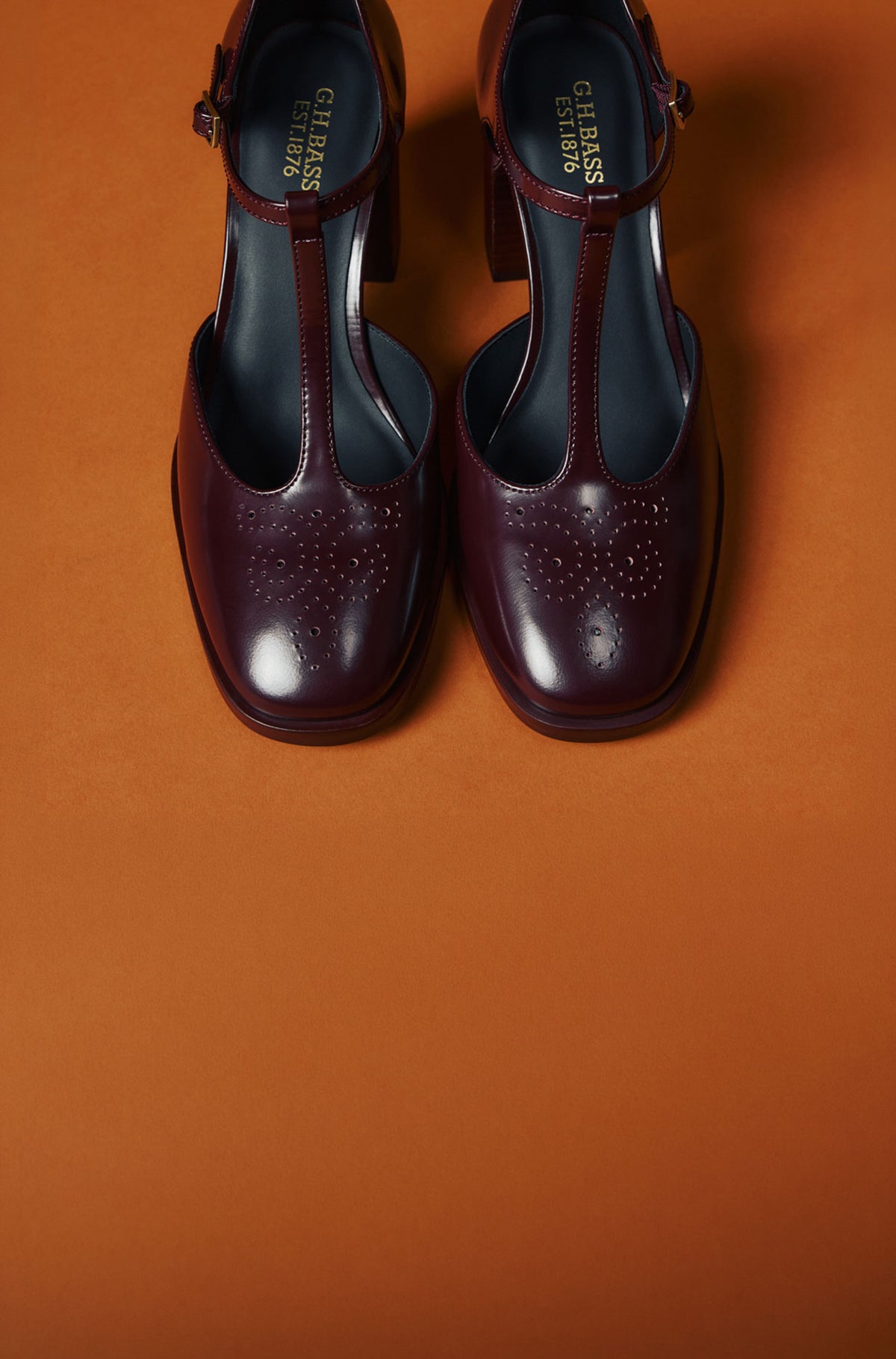A pair of burgundy heeled loafers against an orange background