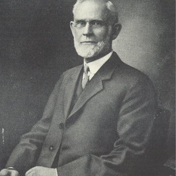 A black and white portrait of a man sitting in a chair wearing a suit and tie