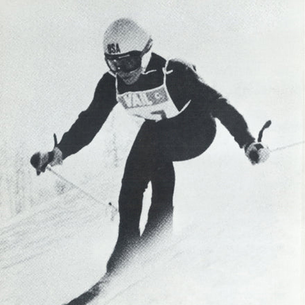 A black and white image of a person skiing down a slope wearing a Team USA helmet