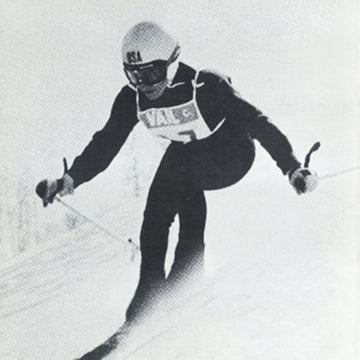 A black and white image of a person skiing down a slope wearing a Team USA helmet