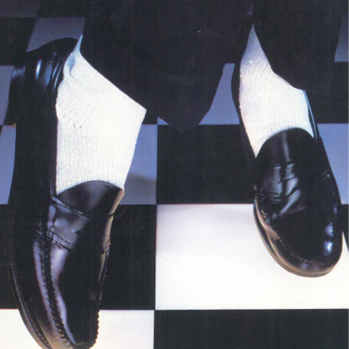 A close-up of a person wearing a pair of black loafers with white socks on a black and white tiled floor