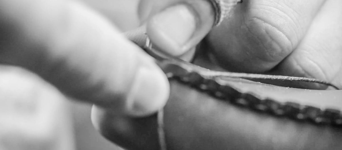 A close-up shot of a person's fingers stitching together a shoe