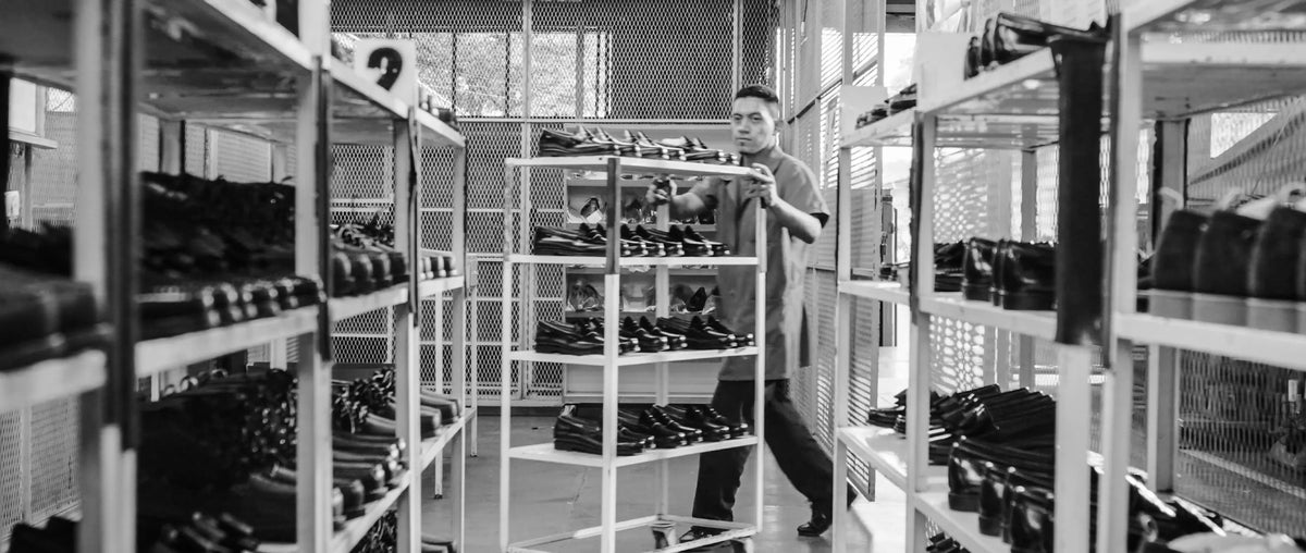 A black and white image of a man pushing a rack of loafers