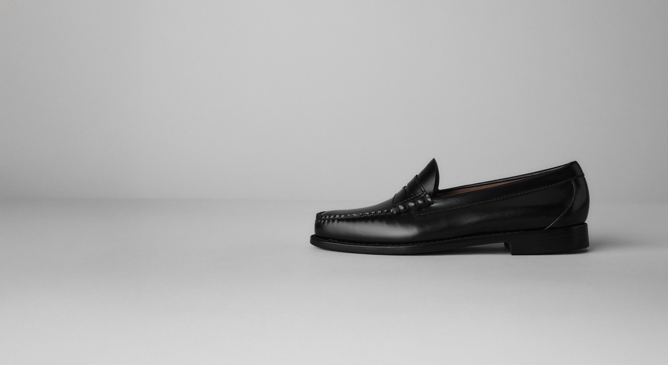 A single black loafer displayed against a light grey background