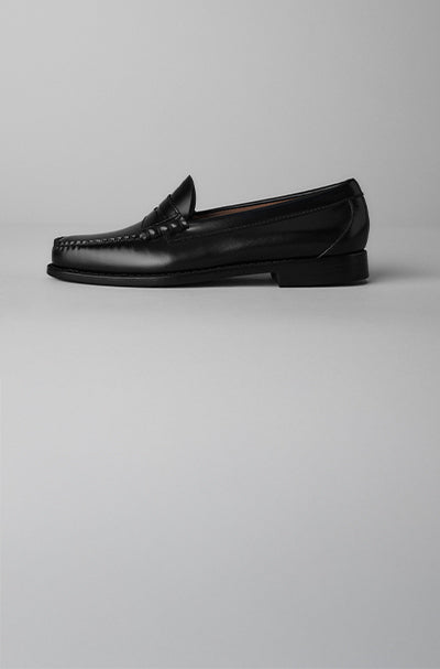 A single black loafer displayed against a light grey background