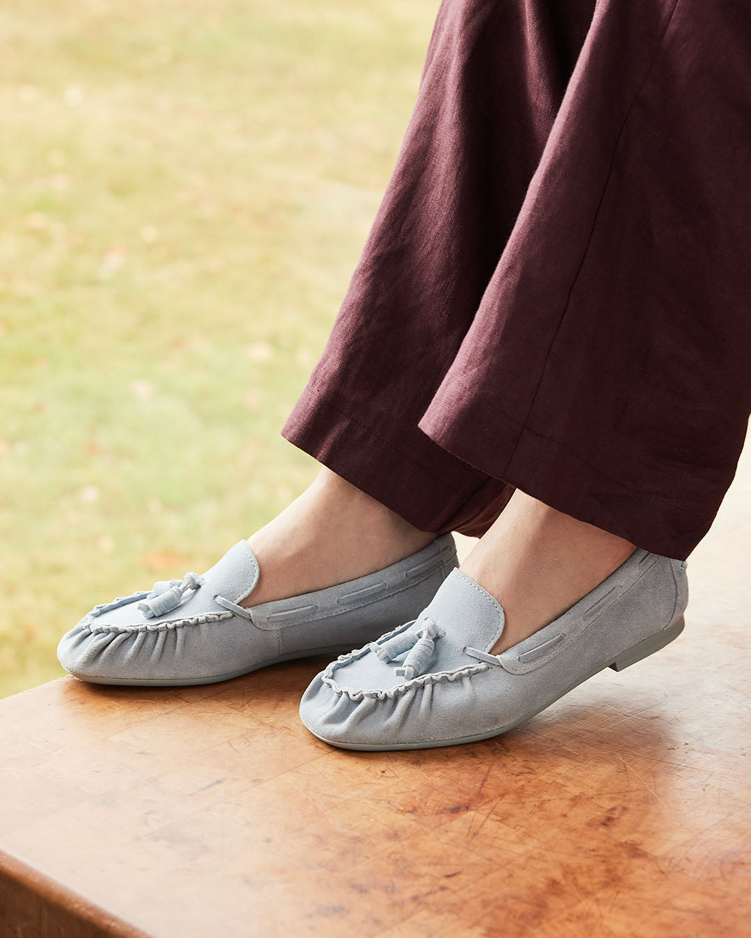 Women sitting on desk with legs crossed wearing baby blue suede loafers.