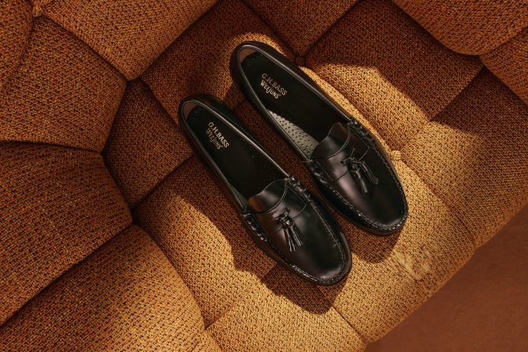 A pair of black tassel loafers on an orange couch