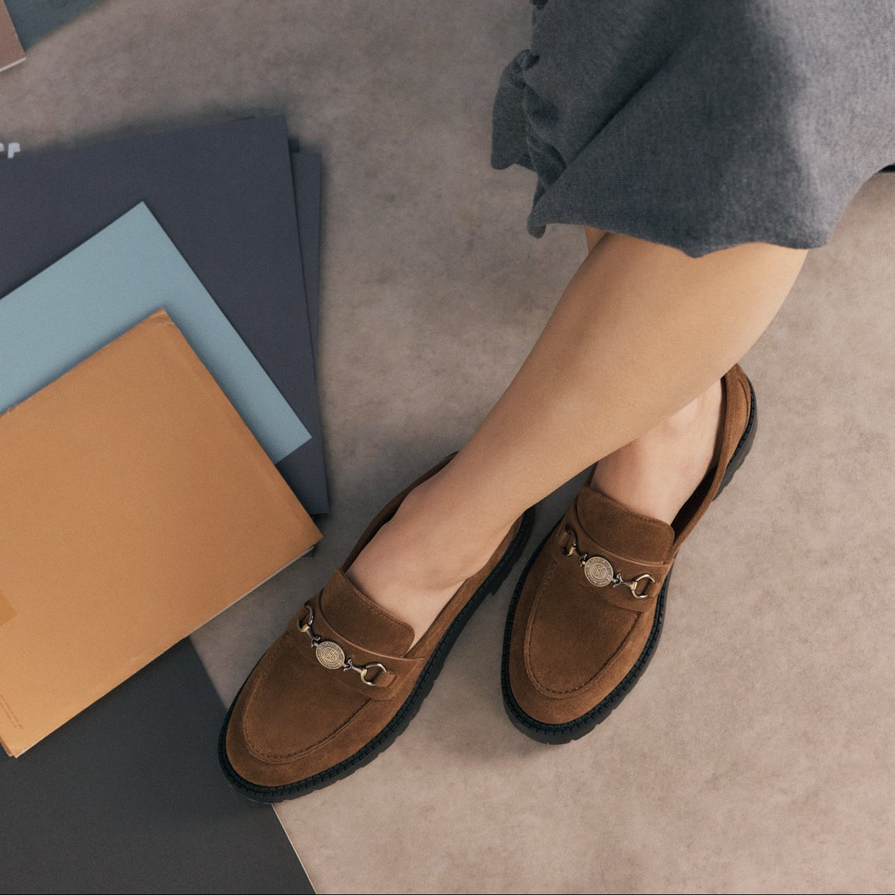 A close-up shot of a woman sitting cross-legged on the floor wearing brown suede loafers 