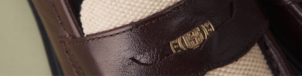 A close-up shot of the branded coin and stitching on a brown and white loafer