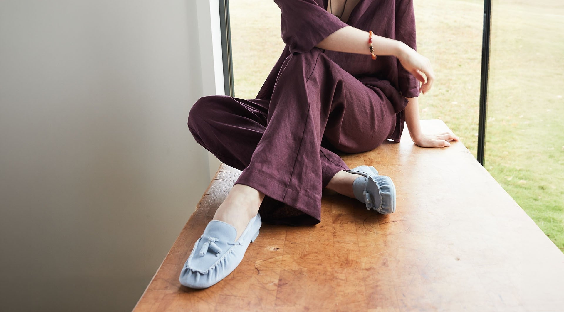 Women sitting on desk with legs crossed wearing baby blue suede loafers.