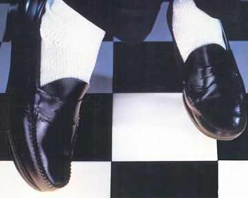 A close up of someone wearing black loafers and white socks against a black and white tiled floor