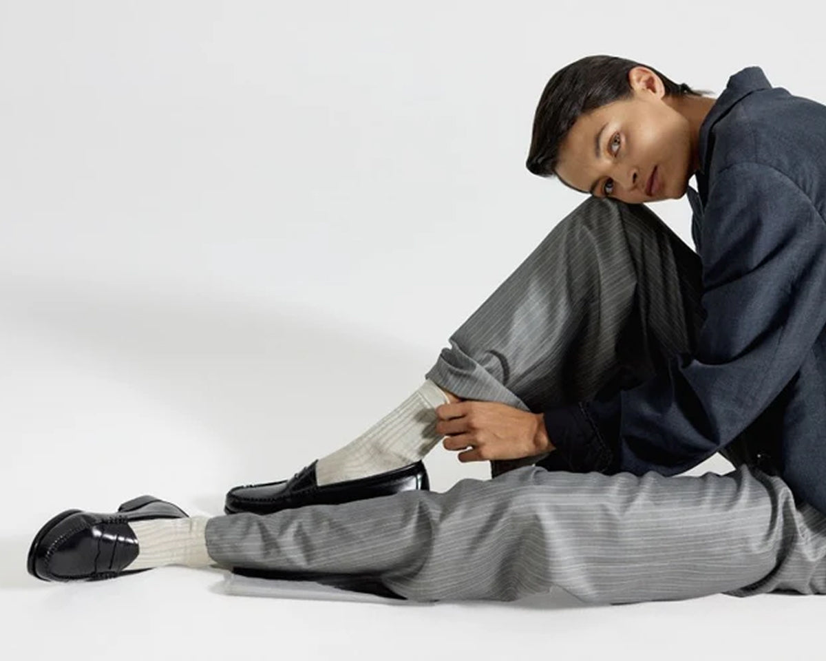 A woman sitting on the floor while leaning her head against her right knee and wearing black loafers