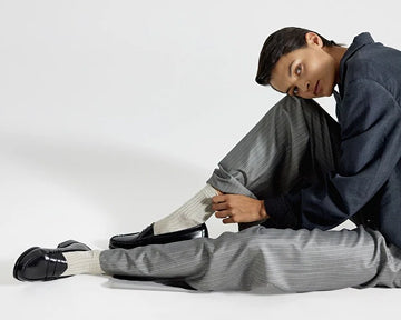 A woman sitting on the floor while leaning her head against her right knee and wearing black loafers