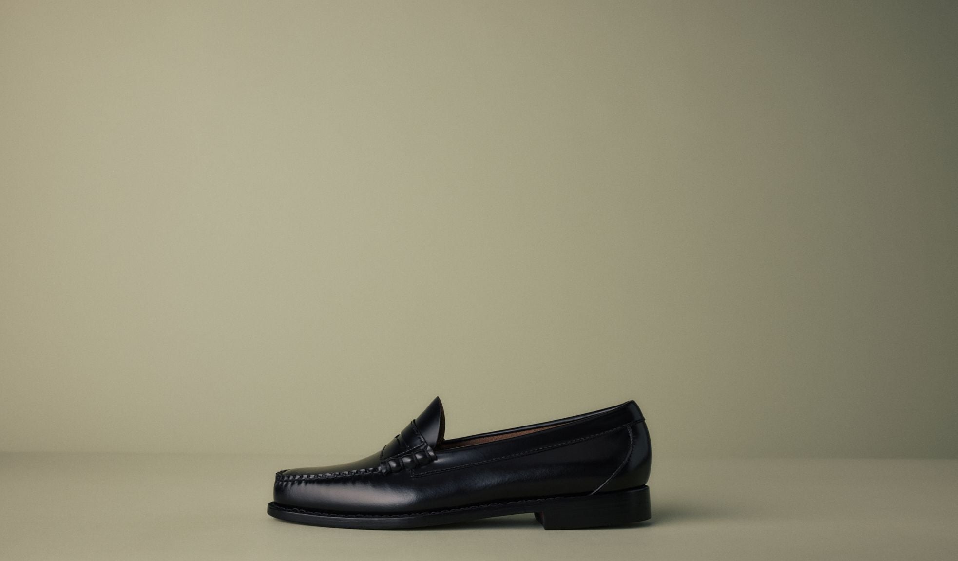 Un seul mocassin noir exposé sur un fond vert pâle